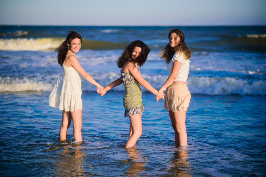 Three sisters holding hands in the ocean on Folly Beach.