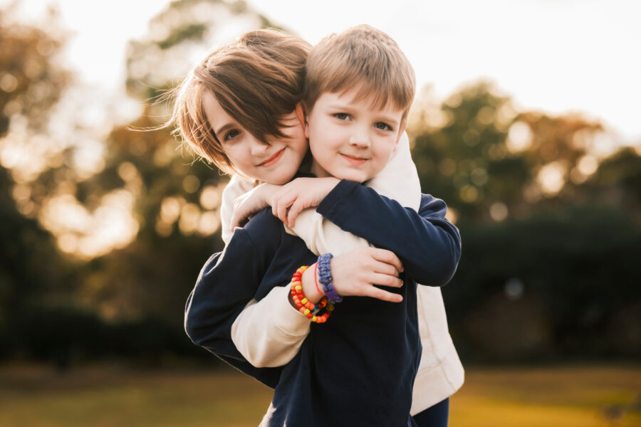 Two children hugging in a park at sunset.