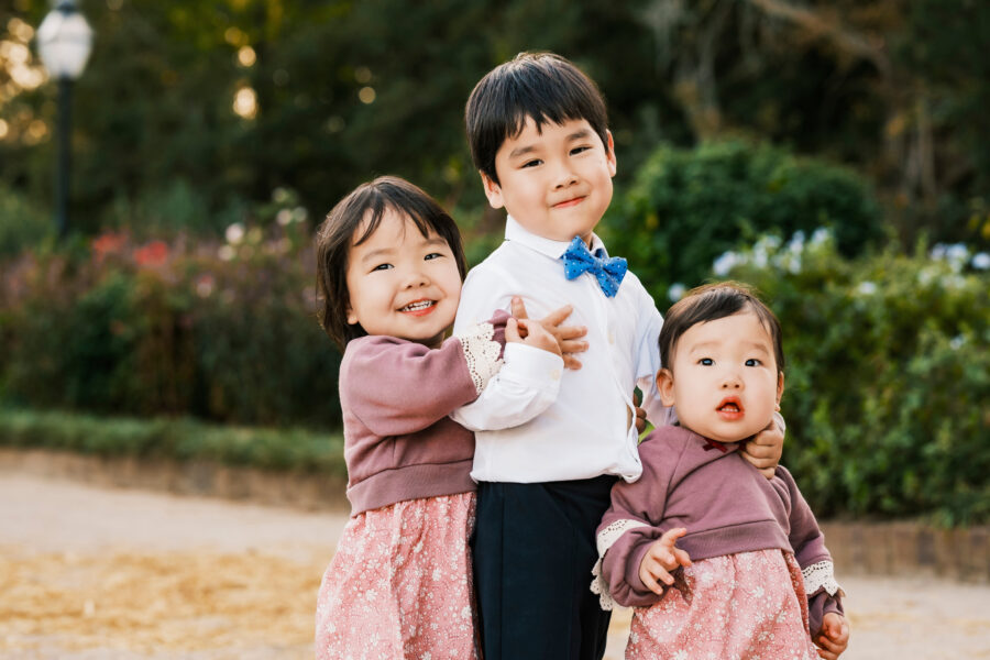 Three young siblings posing together at an outdoor park.