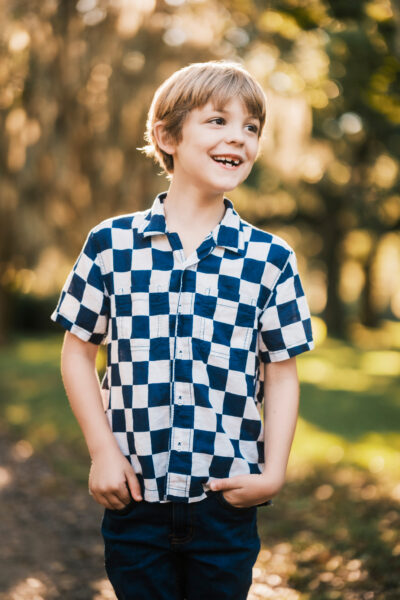 Smiling boy in checkered shirt at outdoor park.
